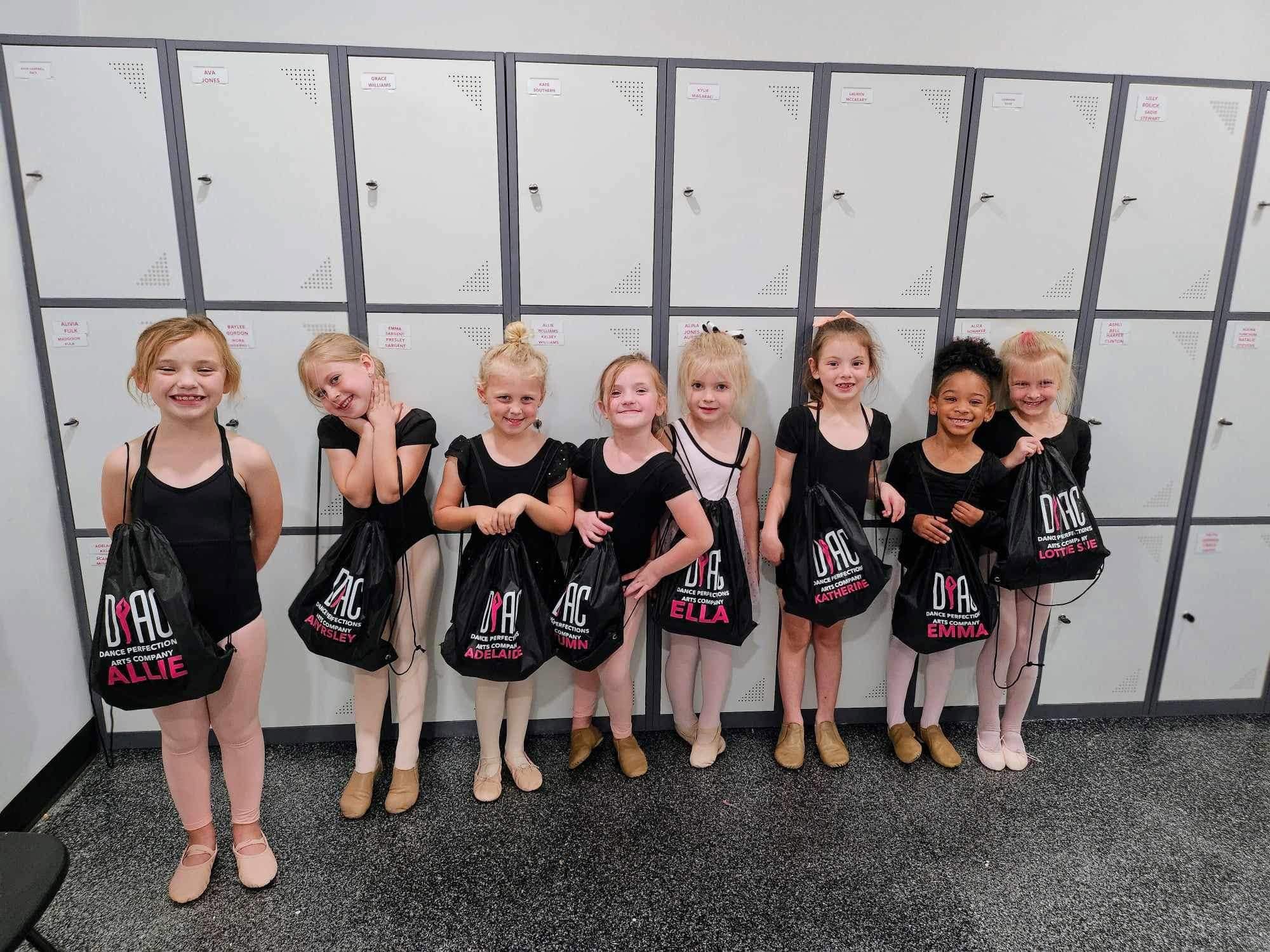 Young dancers with matching dance bags lined up outside the studio lockers