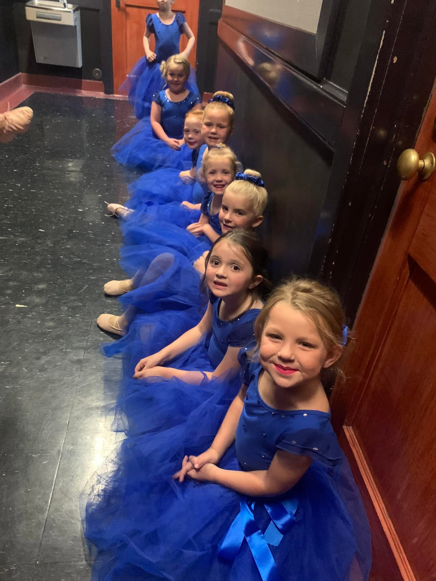 A row of preschool ballerinas in blue tutus waiting backstage before their recital number