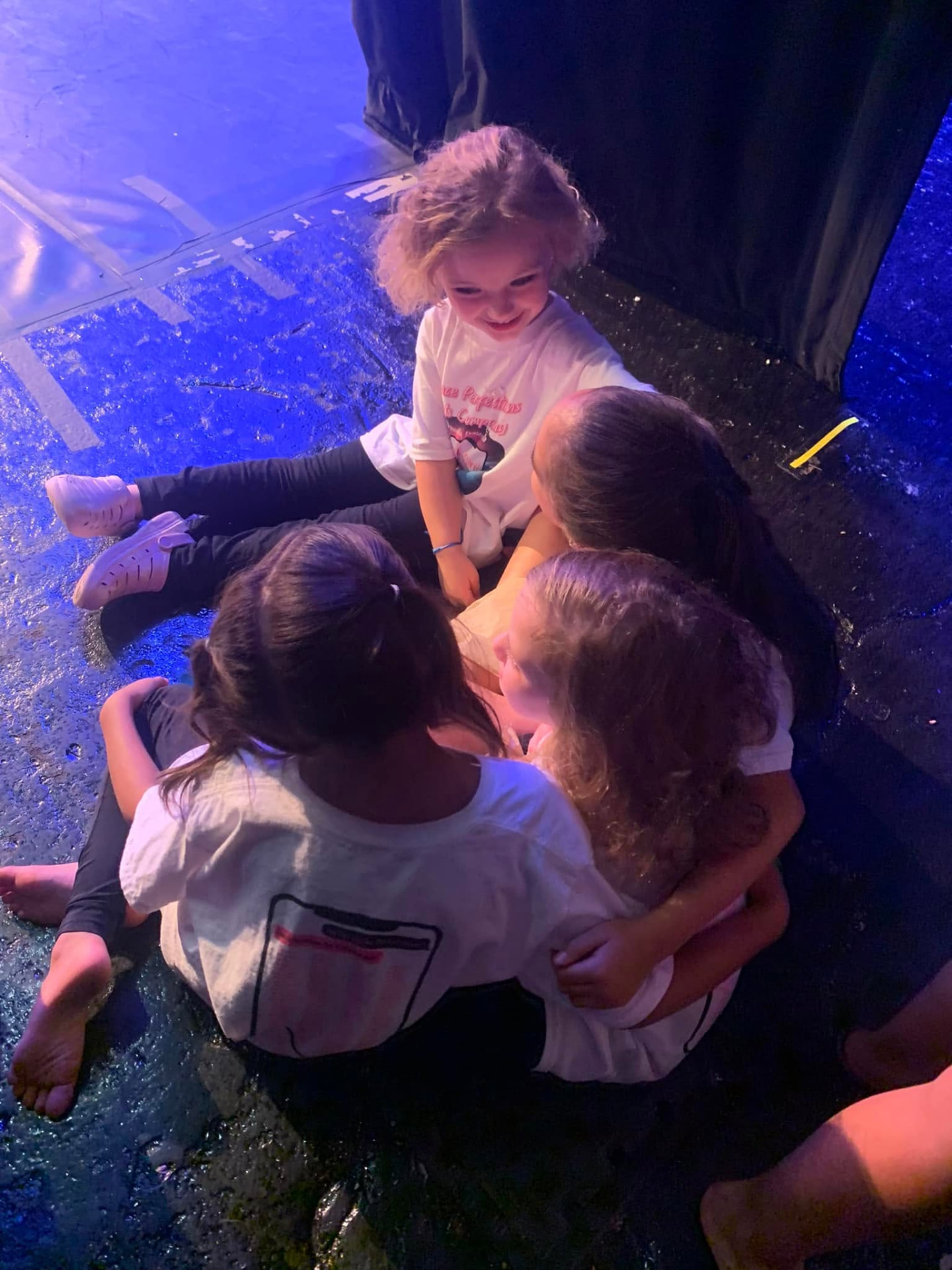 Young dancers in matching white DPAC shirts sitting together backstage in a circle