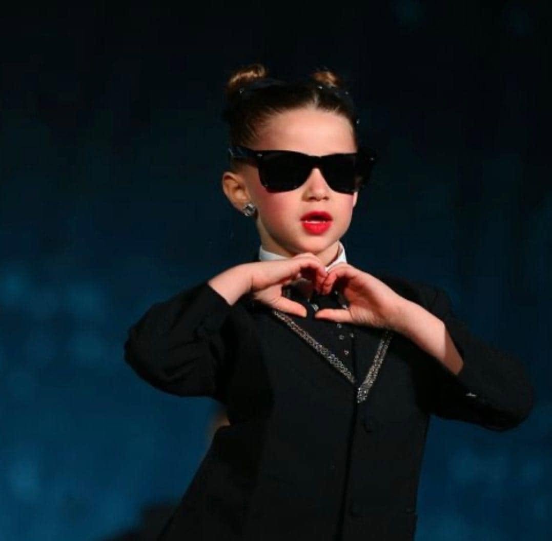 A young Dance Perfections dancer in costume making a heart with her hands on stage