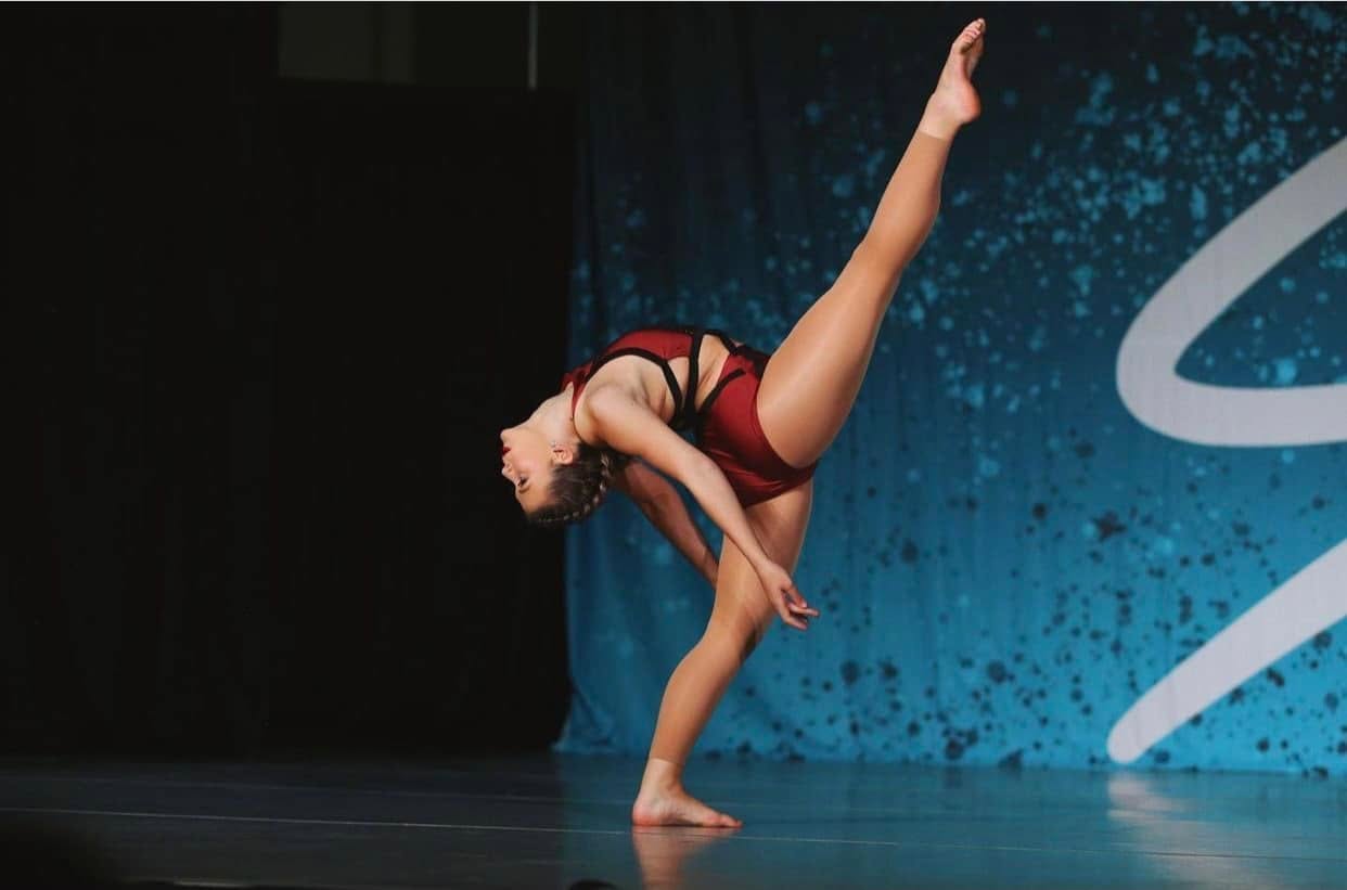 A Dance Perfections dancer performing a dramatic flexed leap on stage