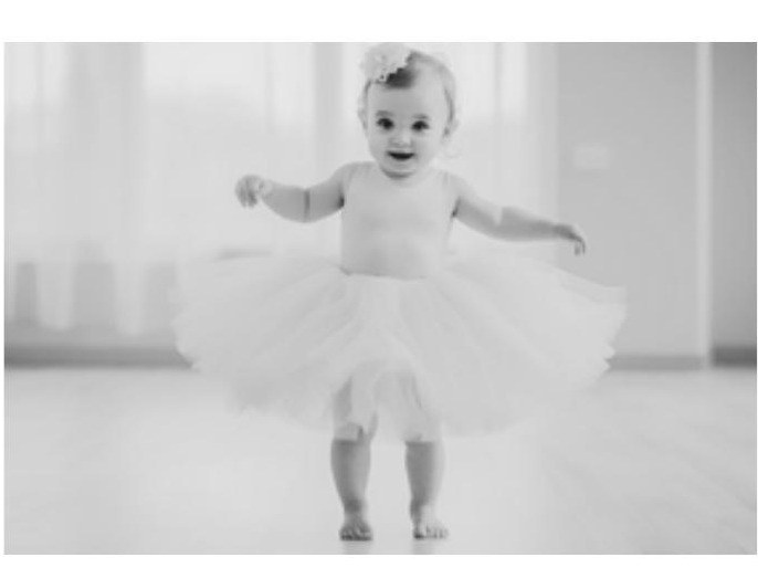 Little one in a white tutu taking her first steps across the studio