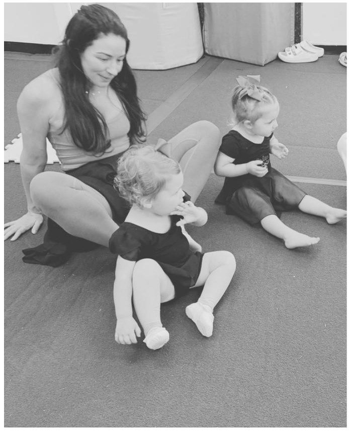 Instructor sitting on the floor guiding two toddlers in ballet class