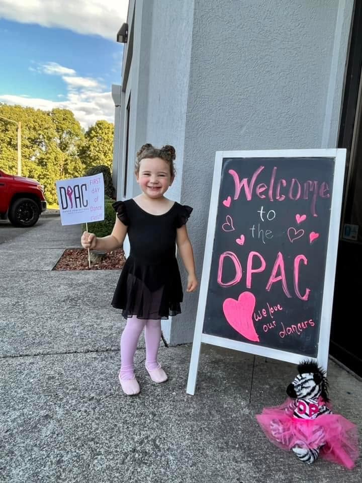 A young dancer beside the Dance Perfections welcome sign on her first day